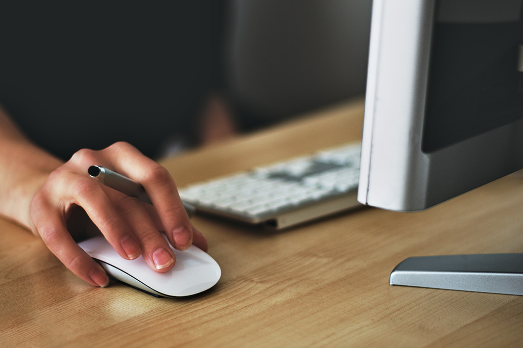 A woman's hand holding a mouse beside a keyboard.