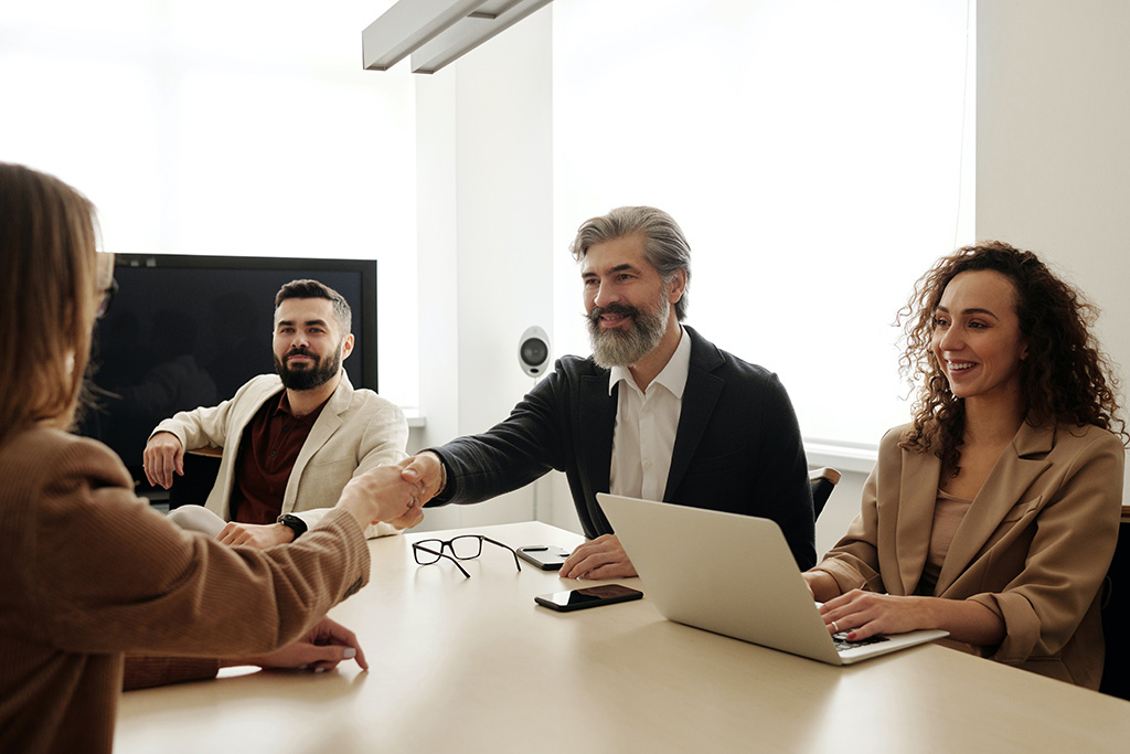 A group of people sitting at a table, two of them are doing a handshake.