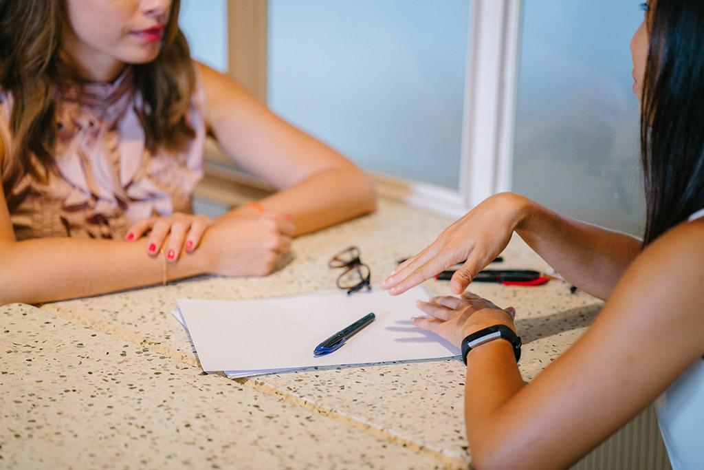 Two women sitting on a table face-to-face.