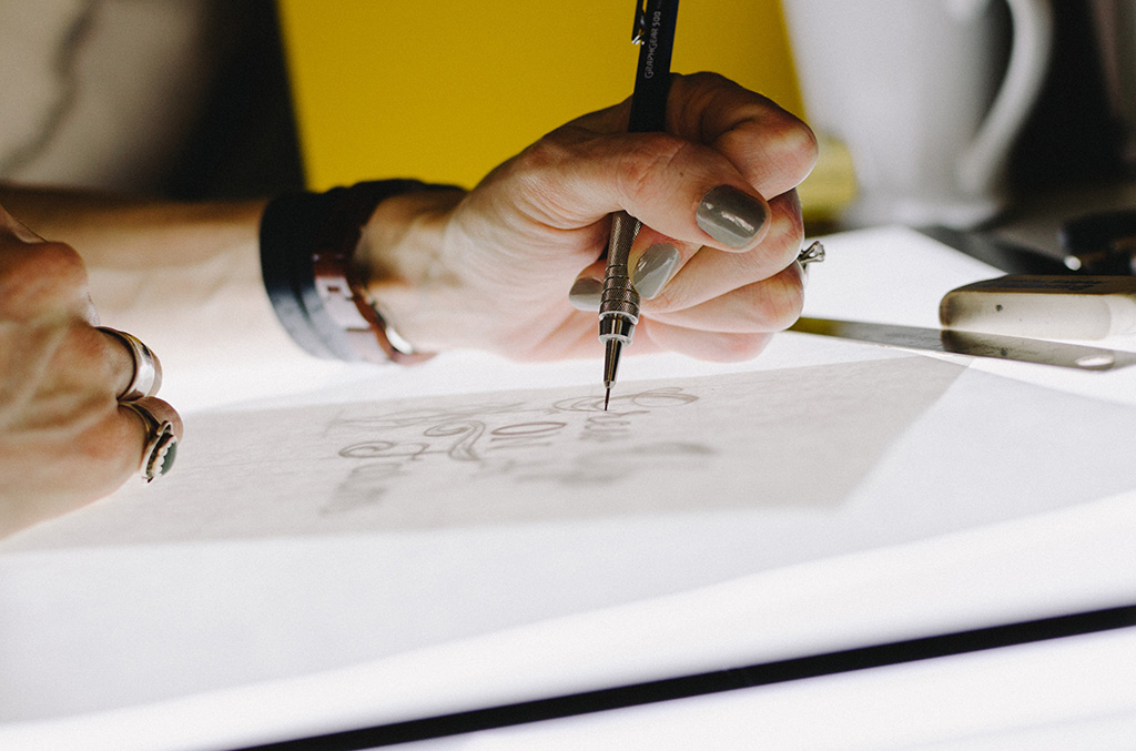 A woman's manicured hand while holding a pen writing calligraphy on a piece of paper